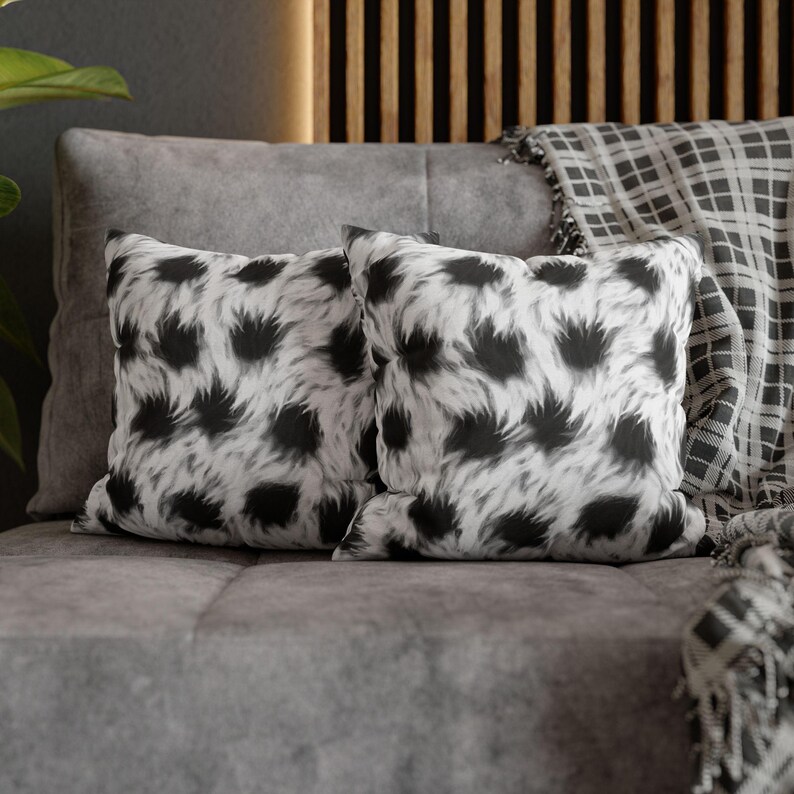 May include: Two black and white patterned throw pillows on a gray couch. The pillows have a fuzzy, animal print design.