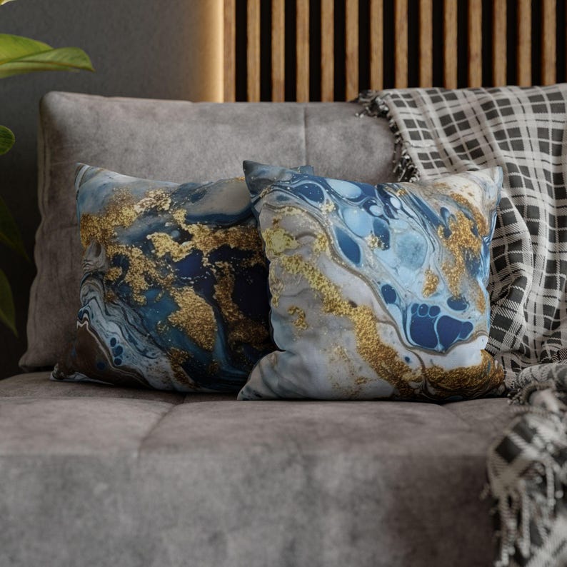 May include: Two decorative throw pillows with a blue, white, and gold marble pattern. The pillows are on a gray couch.