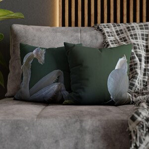 May include: Two throw pillows with a green background and a white praying mantis design. The pillows are on a gray couch with a plaid blanket.