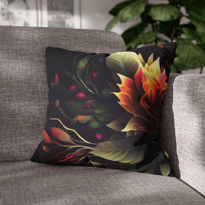 May include: A black throw pillow with a floral design featuring a large, yellow and orange flower with red and green accents. The pillow is on a gray couch.