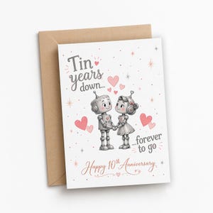 May include: A white greeting card with a brown envelope featuring two illustrated robots holding hands. The text reads Tin years down... forever to go and Happy 10th Anniversary. The design includes pink hearts and small star accents.