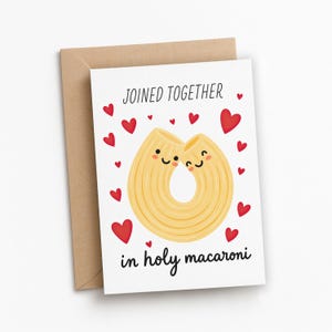 May include: A white card with the words "JOINED TOGETHER in holy macaroni" and illustrations of two smiling pasta shapes and red hearts. The card is accompanied by a brown envelope.
