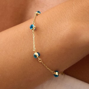 May include: A delicate gold bracelet featuring small, round blue beads. The bracelet is worn on a wrist, with the gold chain and blue beads creating a simple yet elegant design. The bracelet is a piece of jewelry.