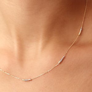May include: A delicate gold chain necklace with three small clusters of beads in different shades of gold.