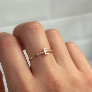 May include: A gold ring with a single sparkling diamond set in the shape of the letter "E".