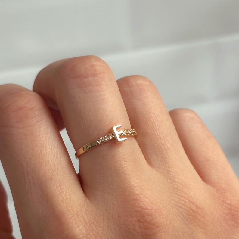 May include: A gold ring with a single sparkling diamond set in the shape of the letter "E".