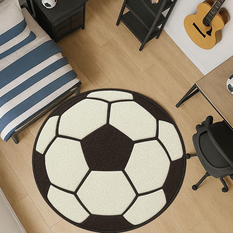 Puede incluir: Una alfombra redonda dise&ntilde;ada para parecerse a un bal&oacute;n de f&uacute;tbol. La alfombra presenta un borde negro con pent&aacute;gonos y hex&aacute;gonos blancos y negros, creando el patr&oacute;n cl&aacute;sico del bal&oacute;n. La alfombra est&aacute; sobre un suelo de madera.