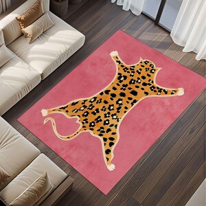Puede incluir: Una alfombra rectangular rosa con un diseño de leopardo estilizado. El leopardo es naranja con manchas negras y un contorno beige claro. La alfombra está sobre un suelo de madera oscura. Dimensiones: aproximadamente 200 cm x 140 cm.