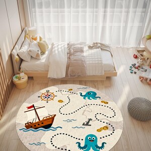 May include: A round, cream-colored children's rug with a nautical theme. The rug features a cartoon ship, compass, octopus, and treasure map design. The rug is placed on a light wood floor in a bedroom setting.