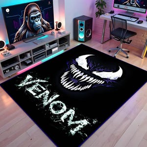 Puede incluir: Alfombra rectangular negra con un gráfico de Venom blanco y morado. La alfombra tiene la palabra "Venom" en texto blanco estilizado. La alfombra está colocada sobre un suelo de madera en una habitación con TV y ordenador.