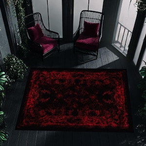 May include: A dark, moody outdoor scene featuring a rectangular rug with a red, textured design. Two black wicker chairs with red cushions are visible, along with a dark wooden deck. The rug is the focal point, adding a pop of color.