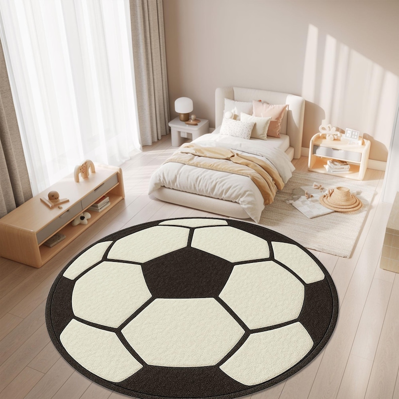 Puede incluir: Una alfombra redonda dise&ntilde;ada para parecerse a un bal&oacute;n de f&uacute;tbol. La alfombra presenta un borde negro y pent&aacute;gonos negros, con hex&aacute;gonos blanquecinos. La alfombra est&aacute; colocada sobre un suelo de madera clara en un dormitorio.