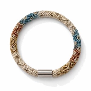 May include: A circular beaded bracelet featuring a repeating chevron pattern in shades of cream, blue, copper, and gold. The bracelet is constructed from tiny, uniform beads and is secured with a smooth, cylindrical silver-toned metal clasp.
