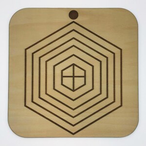 May include: A wooden square with a hole in the top and a concentric pattern of six hexagons etched into the surface.