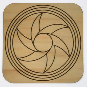 May include: A wooden coaster with a laser-cut design of a circular pattern with concentric circles and a five-pointed star in the center.
