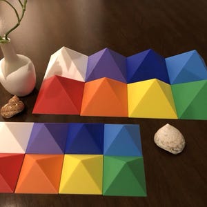 May include: A set of 12 colorful pyramid-shaped blocks arranged in a rainbow pattern. The blocks are made of a smooth, plastic-like material and are perfect for building and stacking.
