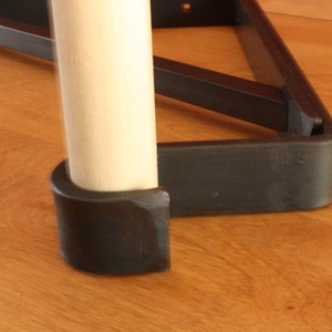 Op de afbeelding: Close-up van een zwart metalen tafelpoot met een houten paal en een zwarte rubberen voet.