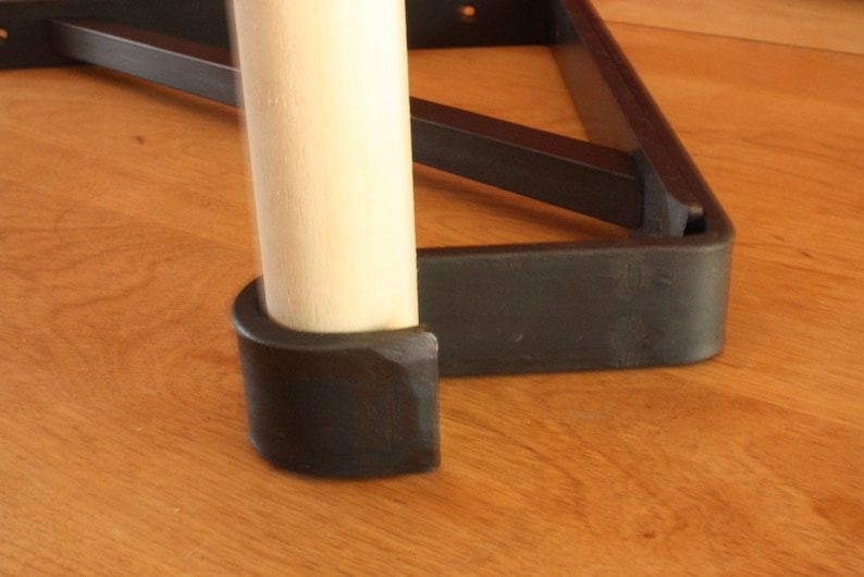 Op de afbeelding: Close-up van een zwart metalen tafelpoot met een houten paal en een zwarte rubberen voet.
