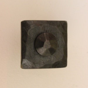 May include: A square, black metal door hinge with a hammered finish. The hinge has a round, black metal pin in the center.