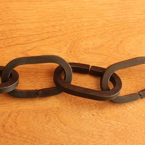 May include: Close-up of a black metal chain with three linked oval-shaped links.