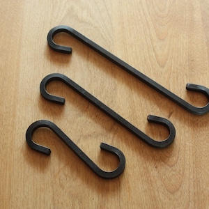 May include: Three black metal S-shaped hooks. The hooks are arranged in a triangular pattern on a wooden surface.