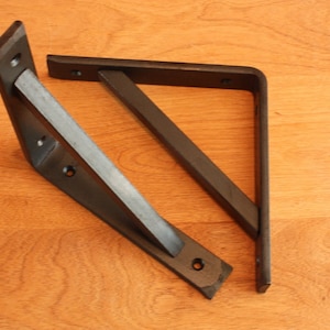 May include: Two black metal shelf brackets, one on top of the other, with a triangular shape and three holes on each bracket.