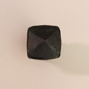 May include: A black metal pyramid-shaped object with a smooth, slightly textured surface.