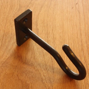 May include: A black metal hook with a square base. The hook is mounted on a wooden surface.