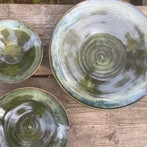 May include: Three ceramic bowls in various sizes with a green glaze and a subtle leaf pattern. The bowls are nested together on a wooden surface.