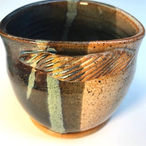 May include: A brown ceramic pot with a speckled glaze and a twisted handle. The pot has a white and brown striped design.