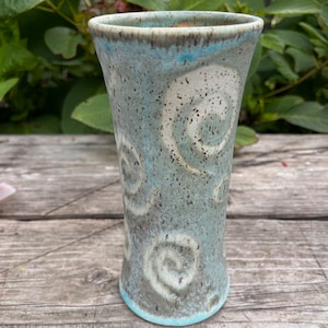 May include: A light blue ceramic vase with a speckled glaze and a white swirl pattern.
