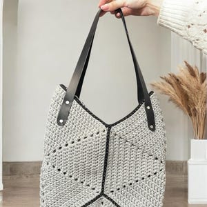 以下が含まれることがあります： 黒い革のストラップと幾何学模様が施されたグレーのクロシェトートバッグ