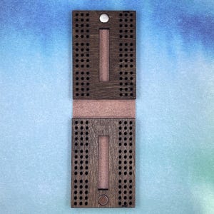 May include: A wooden cribbage board with a brown stain. The board is closed and has a metal latch. The board has a brown felt lining.