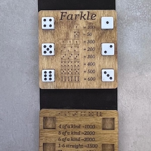 May include: Wooden Farkle dice game board with dice and scoring rules. The game board has the word "Farkle" engraved at the top, along with scoring combinations and point values. Includes a black fabric backing and a cord for hanging.