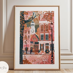 May include: A framed art print depicting a quaint town scene. The artwork features buildings in shades of red and pink, with a clock tower and an American flag. The print is set against a backdrop of autumn foliage.