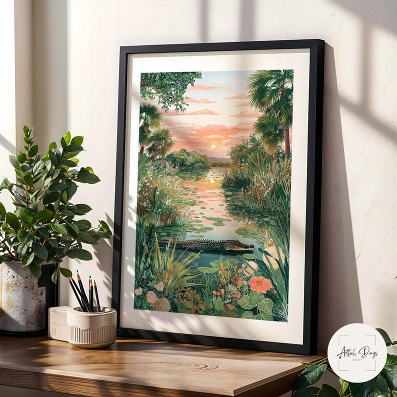 Puede incluir: Una impresi&oacute;n art&iacute;stica enmarcada representa una serena escena de pantano al atardecer. La obra presenta un caim&aacute;n en el agua, rodeado de exuberante vegetaci&oacute;n, nen&uacute;fares y vibrantes flores naranjas. El cielo est&aacute; pintado con c&aacute;lidos tonos de naranja y rosa.