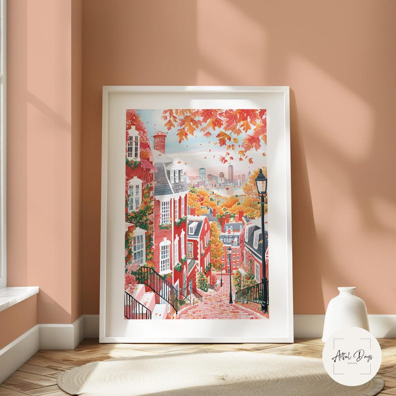 May include: A framed watercolor print of a charming cityscape in autumn. Red brick buildings with white trim line a cobblestone street, with fall foliage in shades of orange and red. A distant skyline is visible under a blue sky.