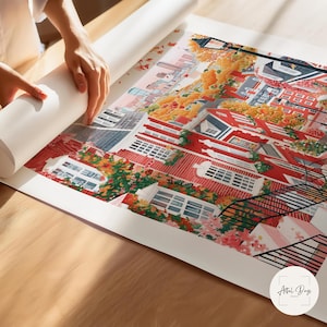 May include: A colorful art print featuring a detailed illustration of a cityscape with red-roofed buildings, lush greenery, and a street lamp. The artwork is being unrolled on a wooden surface. The print has the text "Artful Days" in the bottom right corner.