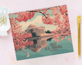 May include: A 2027 U.S. Travel calendar featuring a printed illustration of a white domed building reflected in water, framed by pink cherry blossom branches. The text 2027 U.S. TRAVEL CALENDAR is printed in the lower right corner of the cover.
