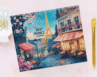 Pode incluir: Um calendário 2027 da França com uma ilustração colorida de uma cena de rua parisiense com a Torre Eiffel, flores cor-de-rosa, um café com toldo e calçadas de pedra. O texto 2027 FRANCE CALENDAR está impresso em preto.