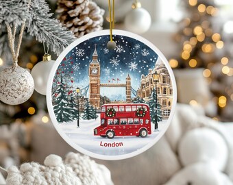 Peut inclure: Ornement de Noël rond représentant une scène hivernale de Londres. Le design comprend Big Ben, le Tower Bridge, un bus à impériale rouge et des flocons de neige. Le mot "London" est imprimé en bas. L'ornement est blanc avec une ficelle dorée.