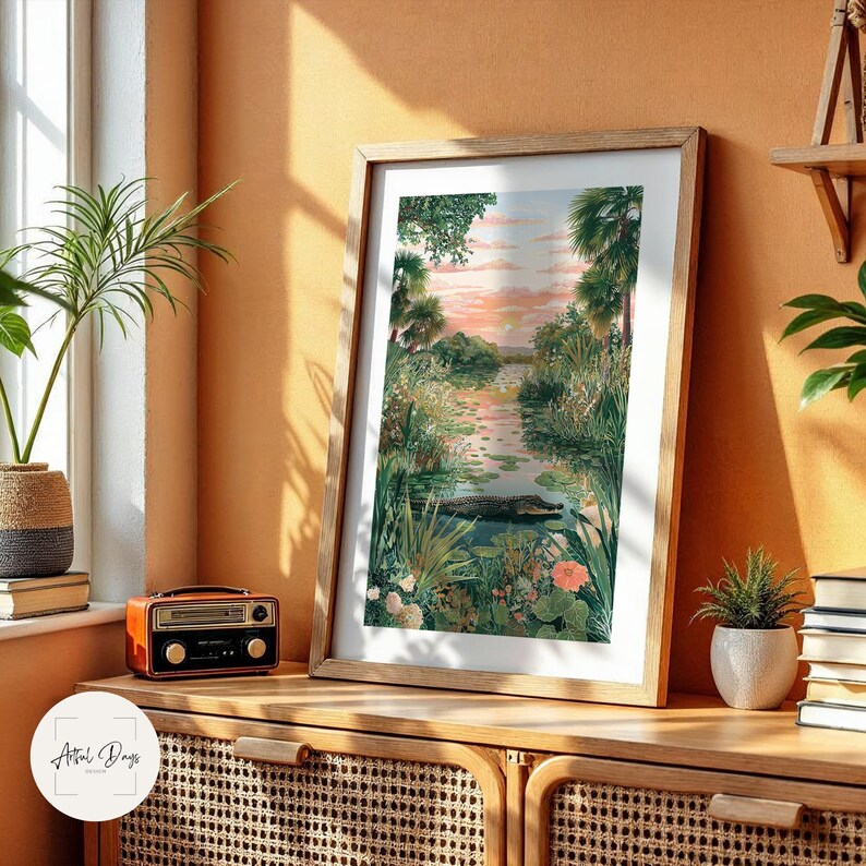 Puede incluir: Una impresi&oacute;n art&iacute;stica enmarcada que presenta un paisaje sereno con un r&iacute;o, exuberante vegetaci&oacute;n y un cielo al atardecer. La obra de arte incluye una representaci&oacute;n de un caim&aacute;n en el agua. La impresi&oacute;n se exhibe en un mueble de madera.