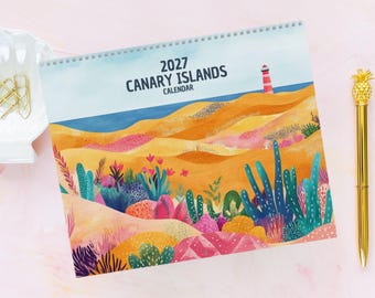 May include: A 2027 Canary Islands calendar with a spiral binding, featuring a colorful illustration of sand dunes, a red and white lighthouse, and various desert plants in shades of orange, pink, blue, and green against a light blue sky.
