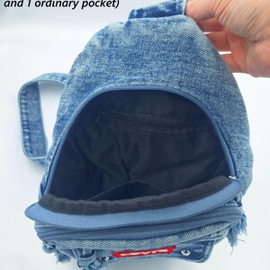 K&ouml;nnte beinhalten: Ein blauer Jeans-Rucksack mit Rei&szlig;verschluss und kleinem Griff. Der Innenraum hat ein schwarzes Futter und zwei Taschen. Der Rucksack hat unten ein rot-wei&szlig;es Logo.