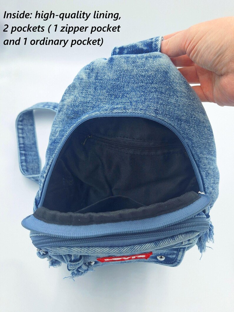 K&ouml;nnte beinhalten: Ein blauer Jeans-Rucksack mit Rei&szlig;verschluss und kleinem Griff. Der Innenraum hat ein schwarzes Futter und zwei Taschen. Der Rucksack hat unten ein rot-wei&szlig;es Logo.