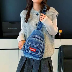 K&ouml;nnte beinhalten: Eine blaue Jeans-Umh&auml;ngetasche mit einer Vordertasche und einem roten "Levis"-Etikett. Die Tasche hat einen einzelnen verstellbaren Riemen und einen Rei&szlig;verschluss. Die Tasche wird &uuml;ber der Schulter getragen.