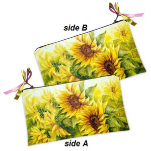 Puede incluir: Dos neceseres rectangulares con un diseño de girasoles. Las bolsas están decoradas con una pintura vibrante de girasoles amarillos y hojas verdes. Cada bolsa tiene una cinta rosa y verde unida a la cremallera.