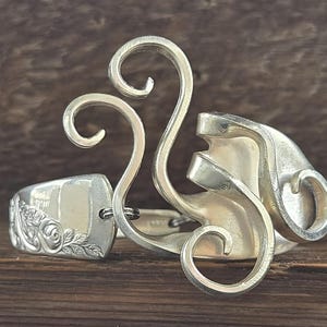 May include: A silver bracelet made from a repurposed spoon, featuring a decorative design of swirling loops and a floral pattern.