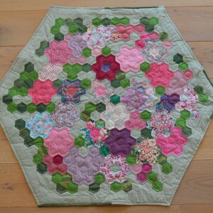 Könnte beinhalten: Ein sechseckiger Quilt mit grünem Hintergrund und einem Muster aus rosa, lila und weißen Blumen. Der Quilt ist aus Stoffresten gefertigt und ein einzigartiges, handgemachtes Stück.