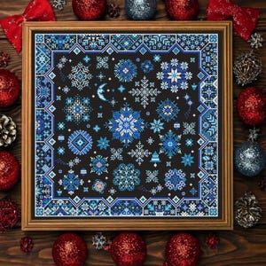 May include: A framed cross-stitch featuring a winter snowflake design in shades of blue and white on a black background. The artwork is surrounded by a wooden frame and festive Christmas ornaments.